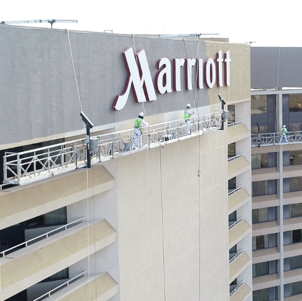 painters on a lift repainting the top of a tall marriott hotel in irving texas