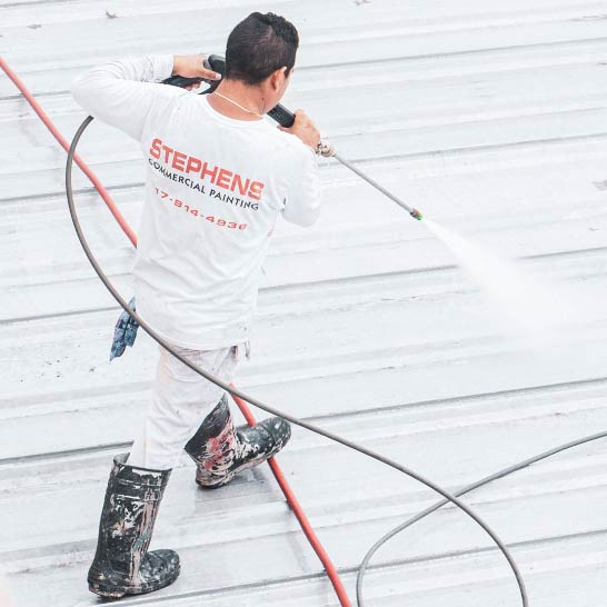 Stephens-Commercial-Painting-Roof-Coatings-Metal-Gallery-Image2-Painter-coats-metal-rooftop Roof Coatings - Stephens Commercial Painting - Painters sprays paint onto metal rooftop